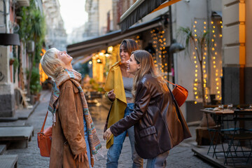 Group of young women laughing and walking in a lively city street with lights at night