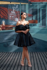 A girl in a short black evening dress walks smiling on the street