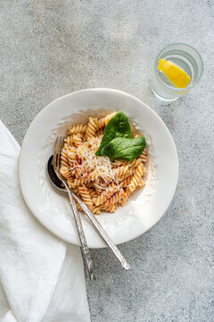 Overhead view of a bowl of fusilli pasta with tomato sauce, spinach and cheese with a glass of lemon water