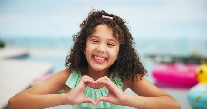 Girl, child and heart hands by swimming pool, happy and funny face for memory, playful and vacation. Kid, smile and comic with sign, emoji and laugh with tongue out, summer and holiday in Costa Rica