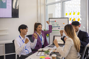 A group of people are gathered around a white board with a woman giving a presentation. Scene is positive and collaborative, as the group is clapping and smiling
