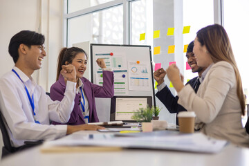 A group of people are gathered around a white board with a woman giving a presentation. Scene is positive and collaborative, as the group is clapping and smiling

