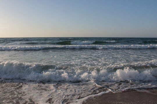 Beach of luxury hotel. sunny day, windy, stormy, wavy sea, blue sky. On the beach shines soft yellow-gold brown-golden sand. Sea waves crashing on the shore with wavy white foam. on island of cyprus
