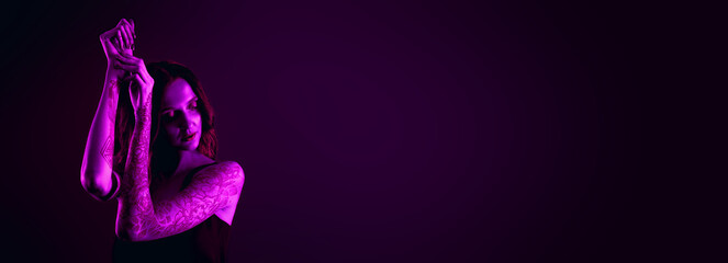 Obraz premium Beautiful woman with tattoos on arms in neon light, space for text. Banner design