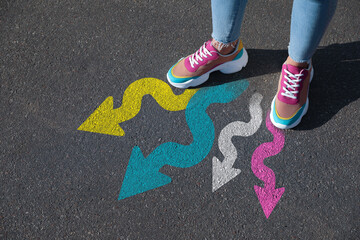 Woman standing near colorful arrows on asphalt road, closeup. Concepts of choice, decision,...