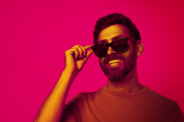Bearded man with stylish sunglasses smiling in neon light, space for text. Banner design