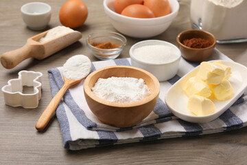 Baking powder in bowl and other products on wooden table, closeup