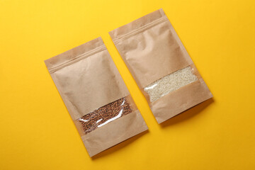 Paper pouch bags with buckwheat and rice on yellow background, top view