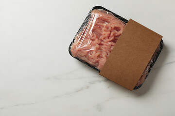 Plastic pack with fresh minced meat on white marble table, top view