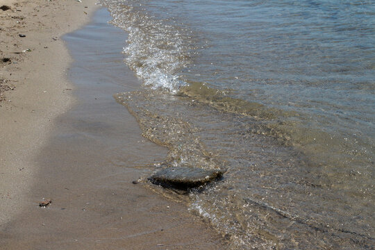 Summer vacation, calm, clean sea water, the view by the sea with waves. Brown yellow sea sand on the beach, bright sun reflecting on big and small sea stones. Balikesir, sarimsakli, T&uuml;rkiye