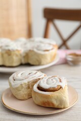Delicious frosted cinnamon rolls on light wooden table indoors, closeup