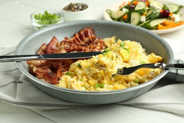 Tasty brunch. Delicious scrambled eggs, bacon and salad served on white wooden table, closeup
