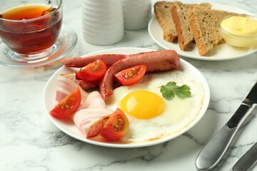 Tasty brunch. Fried egg, sausage, bacon and tomatoes on white marble table, closeup