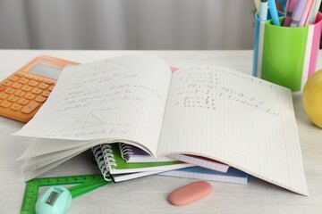 Doing homework. Notebook with assignment and stationery on white desk, closeup