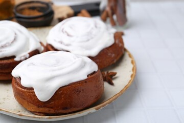 Tasty cinnamon rolls with cream and spices on white tiled table, closeup