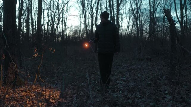 A man shines his flashlight while walking through the forest at night.