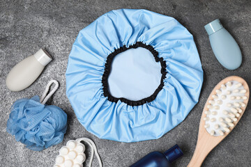Shower cap and bath accessories on grey background, flat lay