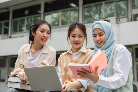 Diverse students smiling while studying with a laptop and notebooks outdoors at a university. - Powered by Adobe