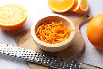 Fresh orange zest in bowl, fruits and grater on grey textured table, closeup