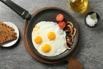 Tasty fried eggs with mushrooms served on grey table, flat lay