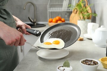 Woman putting tasty fried eggs onto plate from frying pan in kitchen, closeup
