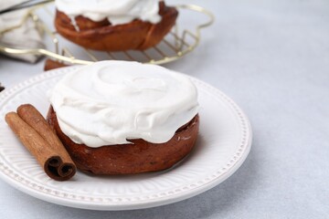 Tasty cinnamon rolls with cream and stick on light table, closeup