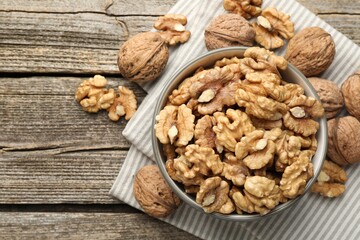 Shelled walnuts in bowl and whole ones on wooden table, flat lay. Space for text