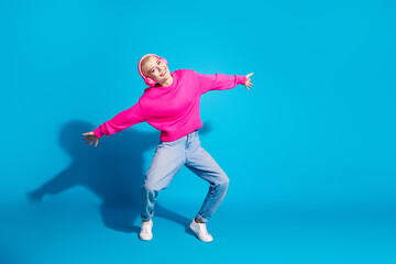 Young woman with short blond hair in casual stylish attire enjoys a joyful moment against a vibrant blue background