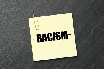 Stop racism concept. Note with strikethrough word on dark grey textured background, top view