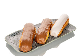 Three eclairs with cream filling on a ceramic saucer, close-up, isolated on a white background.