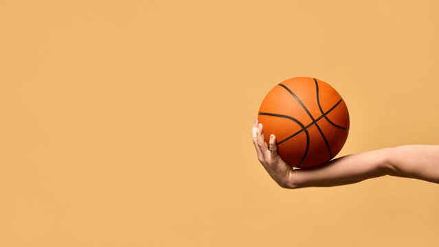 Arm extended outward, gripping basketball firmly, demonstrating stability, technique, and readiness to make powerful play against warm-toned background. Concept of sport equipment, control, strategy.