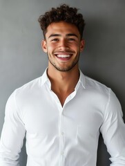 Obraz premium Handsome Young Man Smiling Confidently in White Shirt Against Grey Background