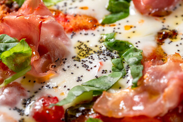 Primo piano di pizza italiana condita con prosciutto cotto, mozzarella, sugo, basilico e semi di papavero 