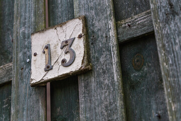 Rusty number 13 and white plate on a rough raw green wooden fence mounted with screws
