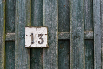Rusty number 13 and white plate on a rough raw green wooden fence mounted with screws
