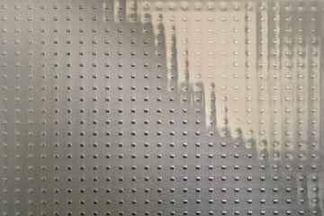 Close-up of textured glass with a repeating pattern of raised lines and dots, creating a...