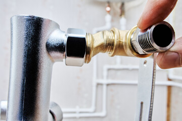 Close-up of hand installing reducer on brass T-fitting, part of plumbing assembly.