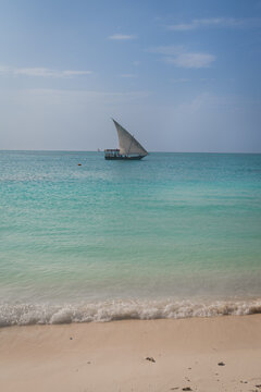 fishing boat, dhow or felucca sailing on the horizon of tropical blue sea and waves on the beach