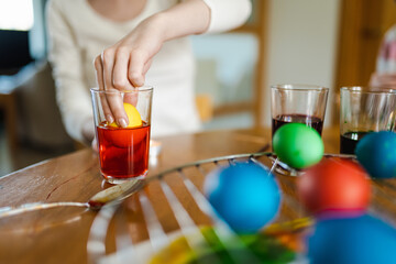Pretty teenage girl dyeing Easter eggs at home. Child painting colorful eggs for Easter hunt. Kid getting ready for Easter celebration.