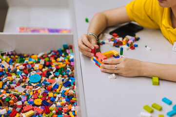 A young teenage girl assembles a construction set from plastic parts and blocks with her hands.
