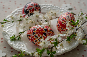 Homemade handmade painted Easter eggs on white plate on spotted tablecloth decorated with...