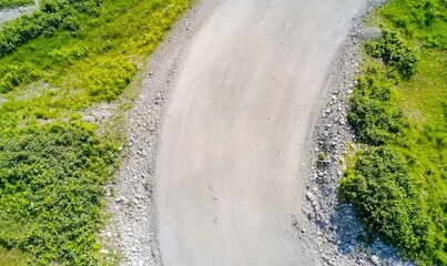 An aerial view of a curved road surrounded by lush greenery and rocky terrain, showcasing nature's beauty and tranquility.