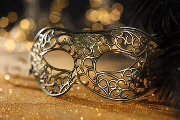 Beautiful carnival mask and black feathers on golden background against blurred lights, closeup. Bokeh effect
