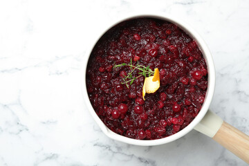 Tasty cranberry sauce in saucepan on white marble table, top view. Space for text