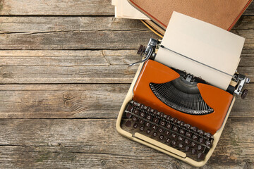 Vintage typewriter with sheet of paper and bag on wooden table, top view. Space for text