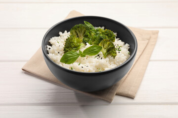 Tasty rice with broccoli and basil in bowl on white wooden table, closeup