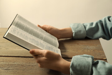 Fototapeta premium Woman reading Holy Bible in English language at wooden table, closeup