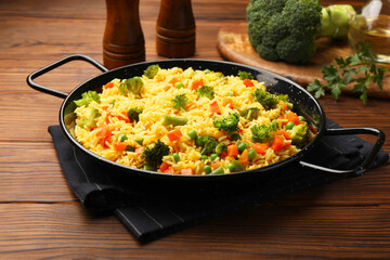 Tasty rice with vegetables in baking dish on wooden table, closeup