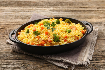 Tasty rice with vegetables in baking dish on wooden table