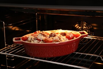 Uncooked pasta casserole with cheese, tomatoes and minced meat in baking dish in oven, closeup